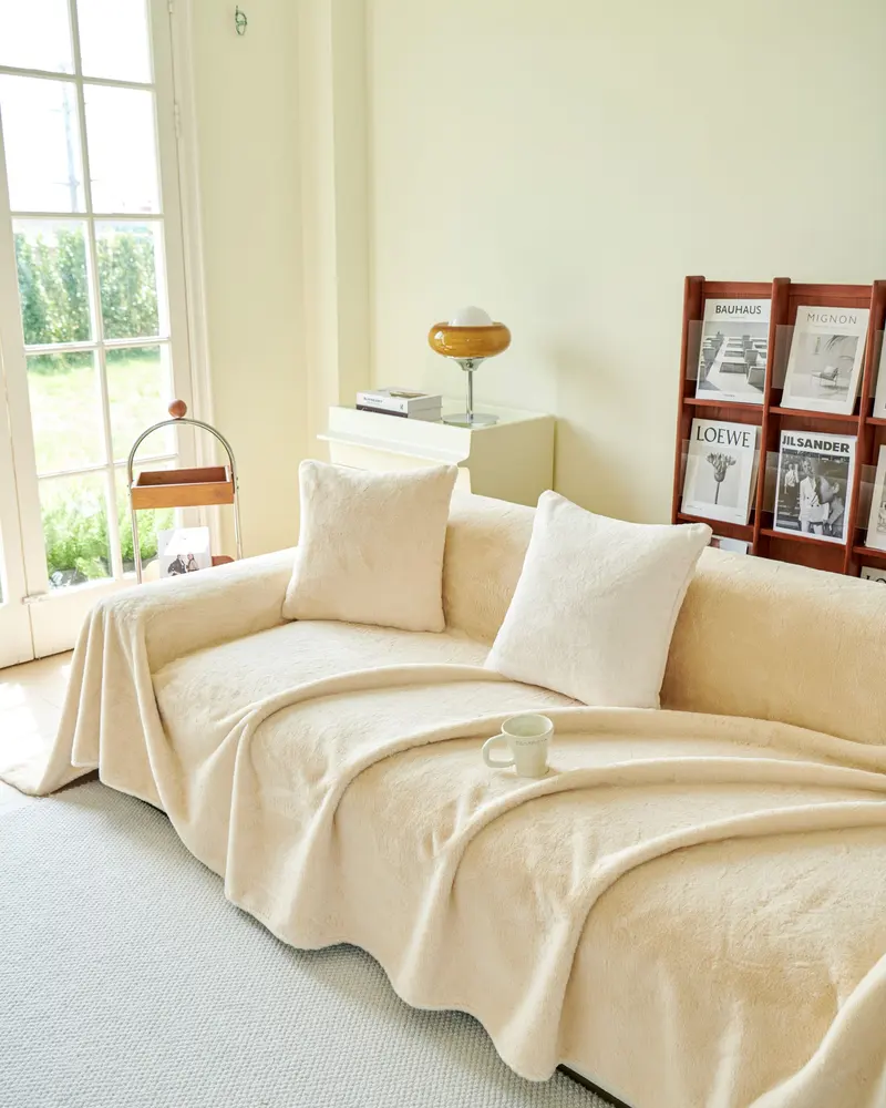 Ljust vardagsrum med beige soffa, filt och kuddar intill ett fönster