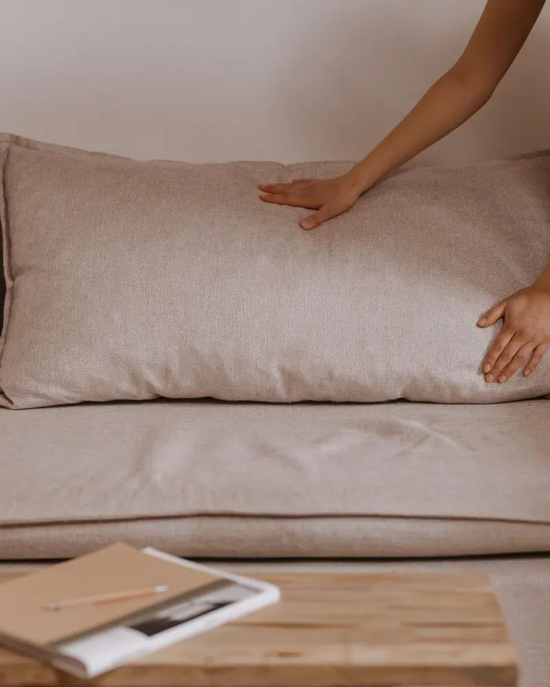 Händer som rättar till en kudde på en beige soffa